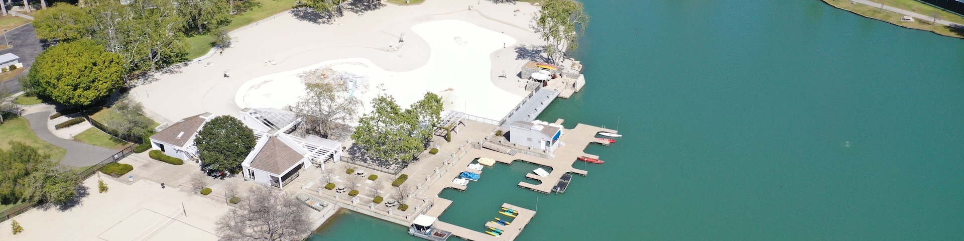 Un parque junto al lago con cancha de tenis, muelle para embarcaciones y edificios residenciales al fondo.
