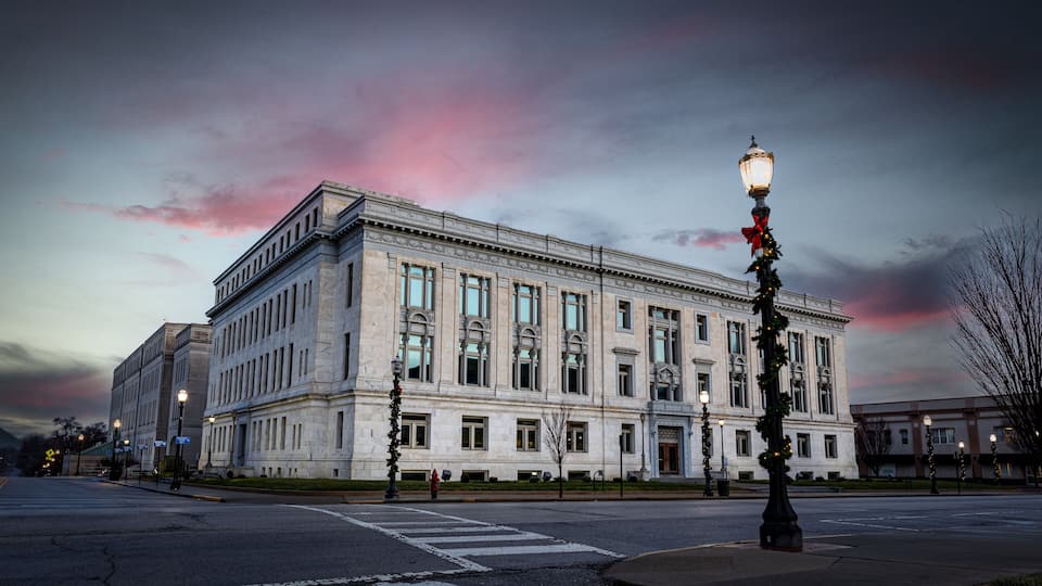 A large, classical building with a symmetrical facade, large windows, and a street lamp with a red bow.