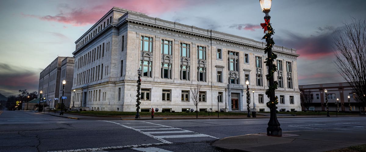 A large, classical building with a symmetrical facade, large windows, and a street lamp with a red bow.