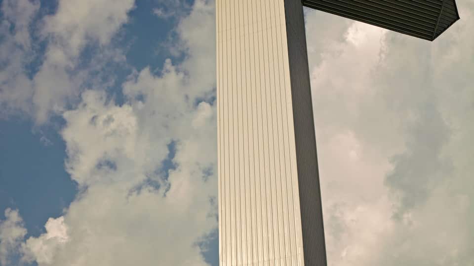 A tall, white, vertical structure with a cross-like design against a partly cloudy sky.