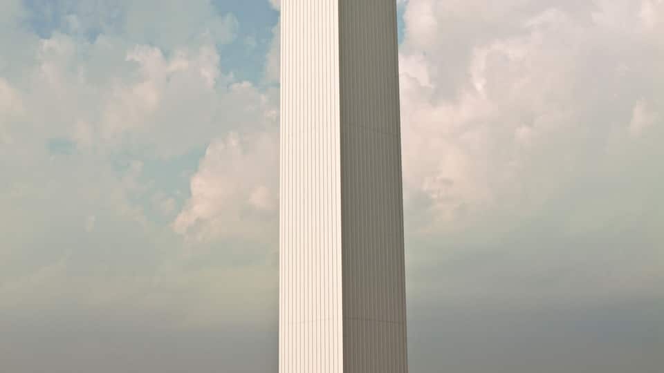 A large white cross-shaped monument with a flagpole at its base, set against a partly cloudy sky.