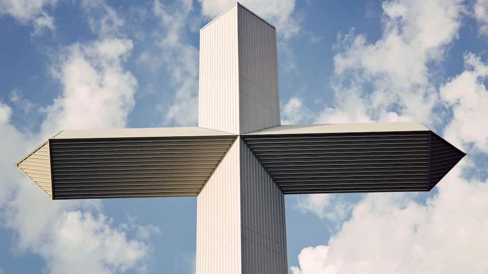 A large, white cross-shaped structure against a blue sky with clouds.