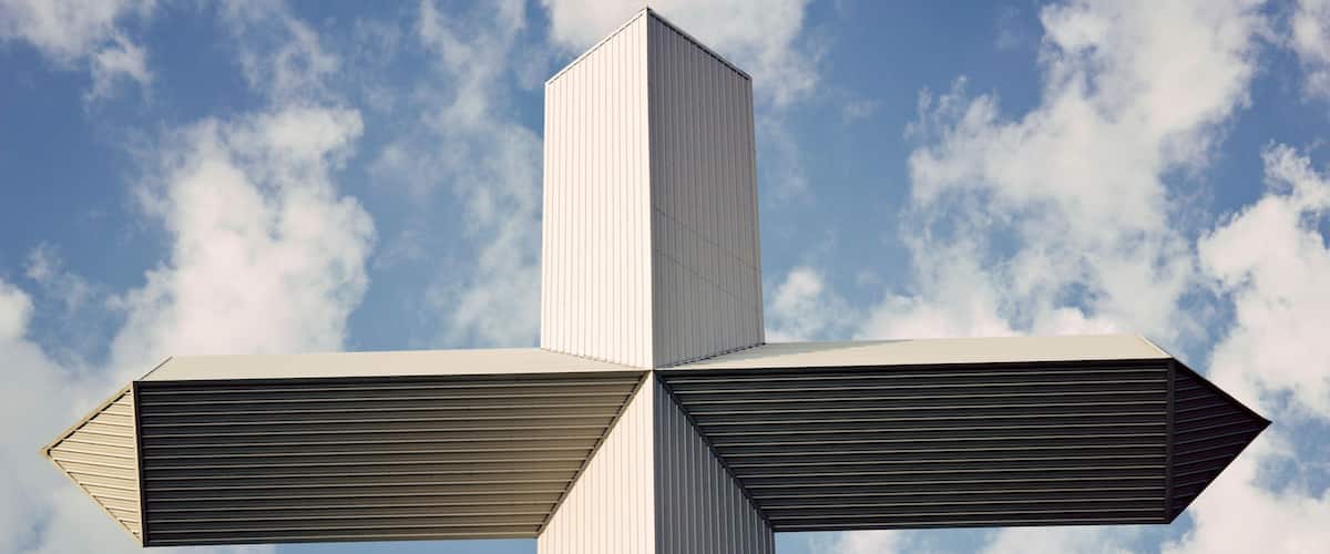 A large, white cross-shaped structure against a blue sky with clouds.