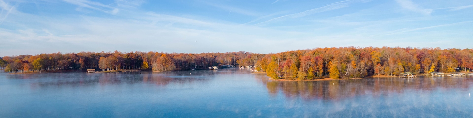 A calm lake with autumn foliage reflecting in the water, surrounded by trees with red, orange, and yellow leaves.
