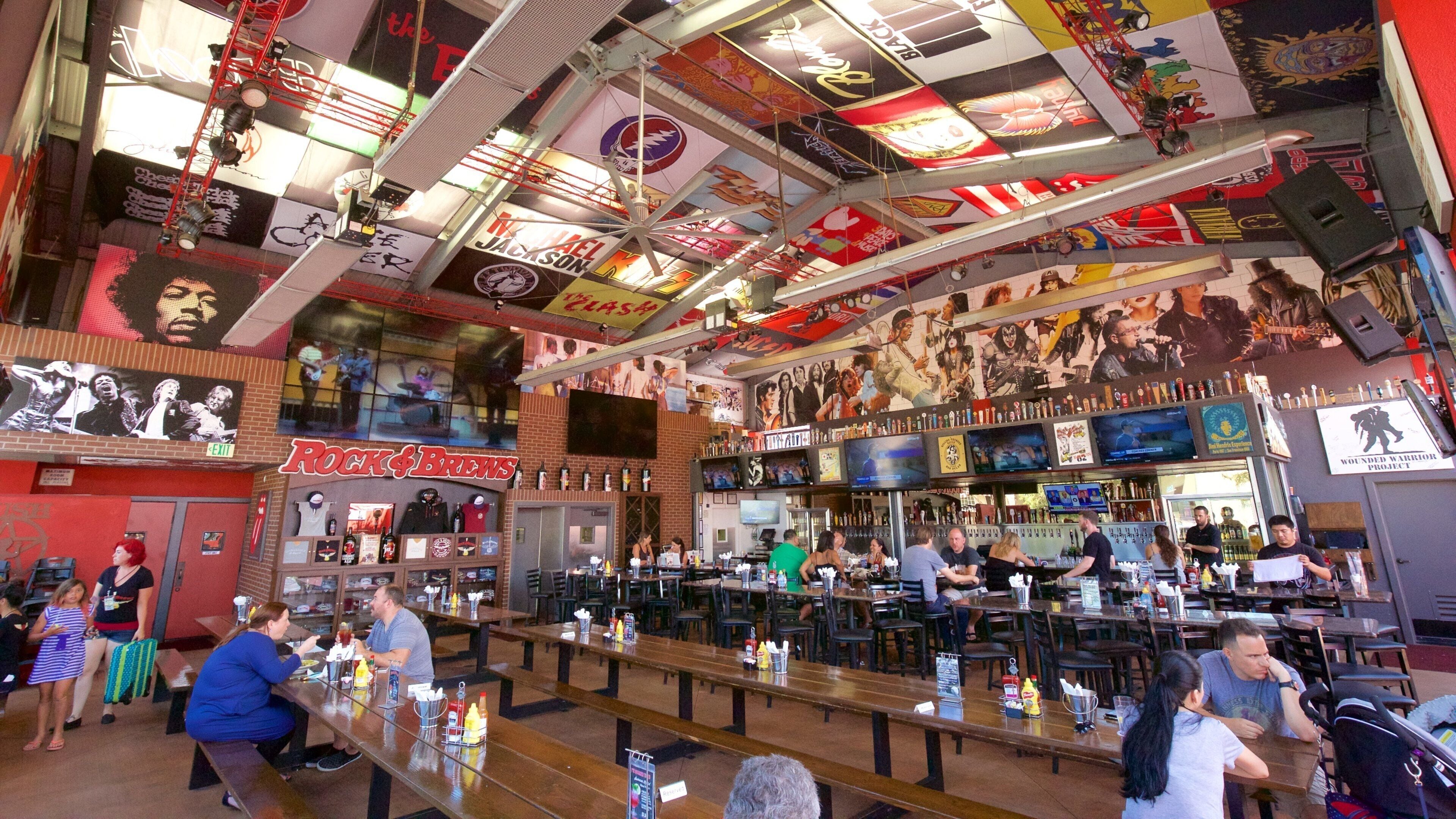 A crowded bar with a high ceiling decorated with posters and a large mural.