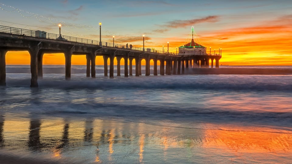 A pier with a dome structure, waves crashing against it, and a sunset in the background.