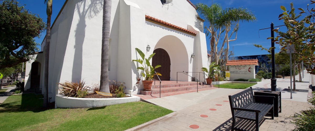 A white church with a red-tiled roof, surrounded by palm trees and a paved walkway.