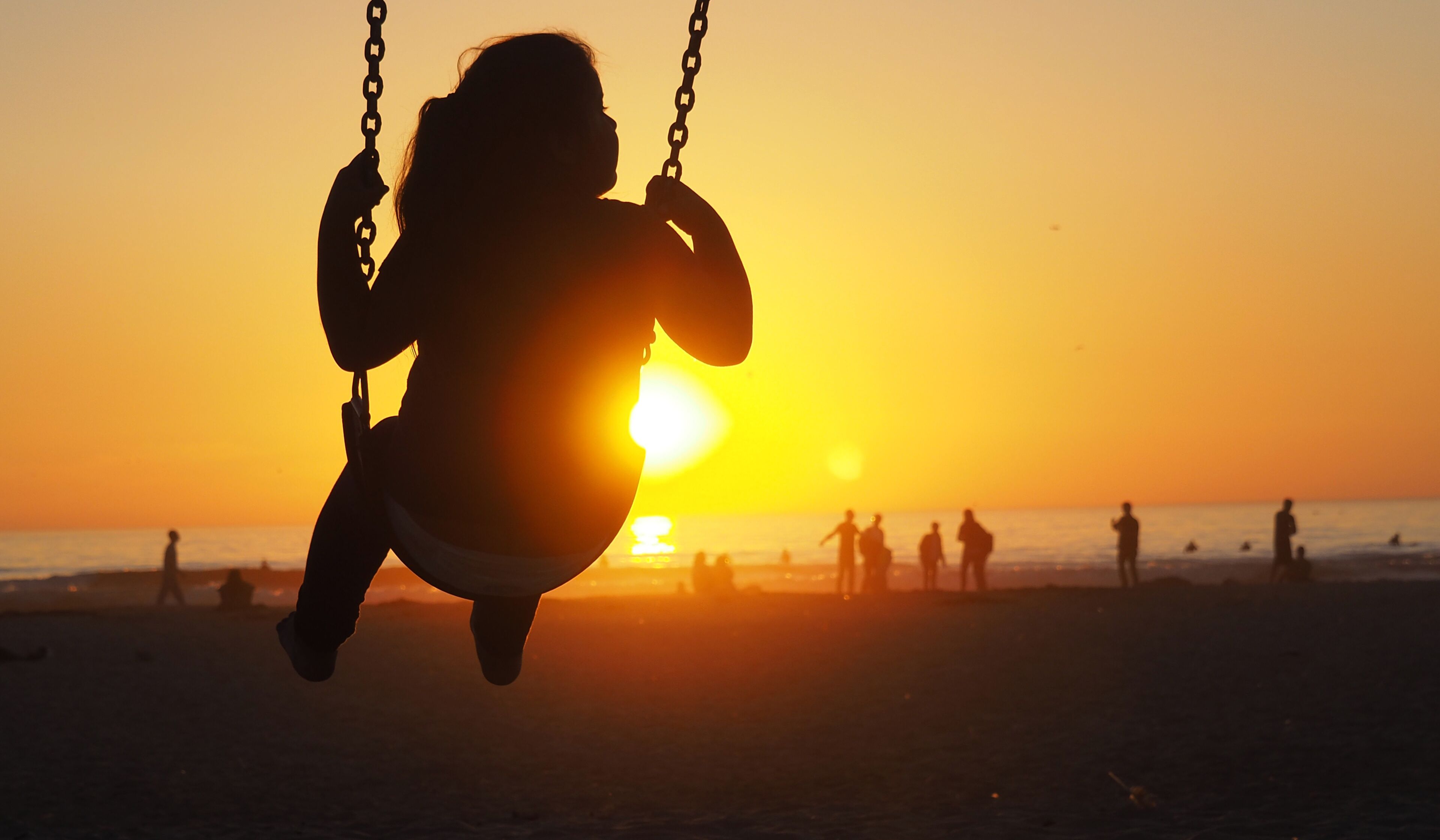 A silhouette of a person on a swing against a sunset at the beach.