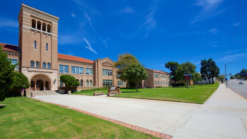 A large brick building with arched windows and a red-tiled roof, surrounded by well-maintained lawns and trees.