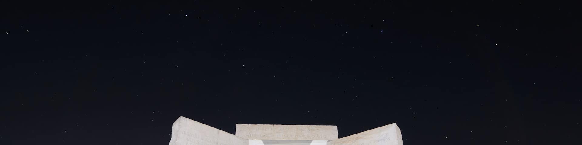 A large stone monument with inscriptions, set against a night sky with stars.