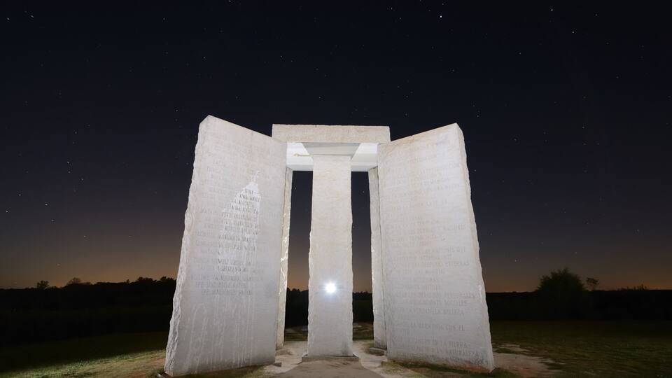 A large stone monument with inscriptions, set against a night sky with stars.