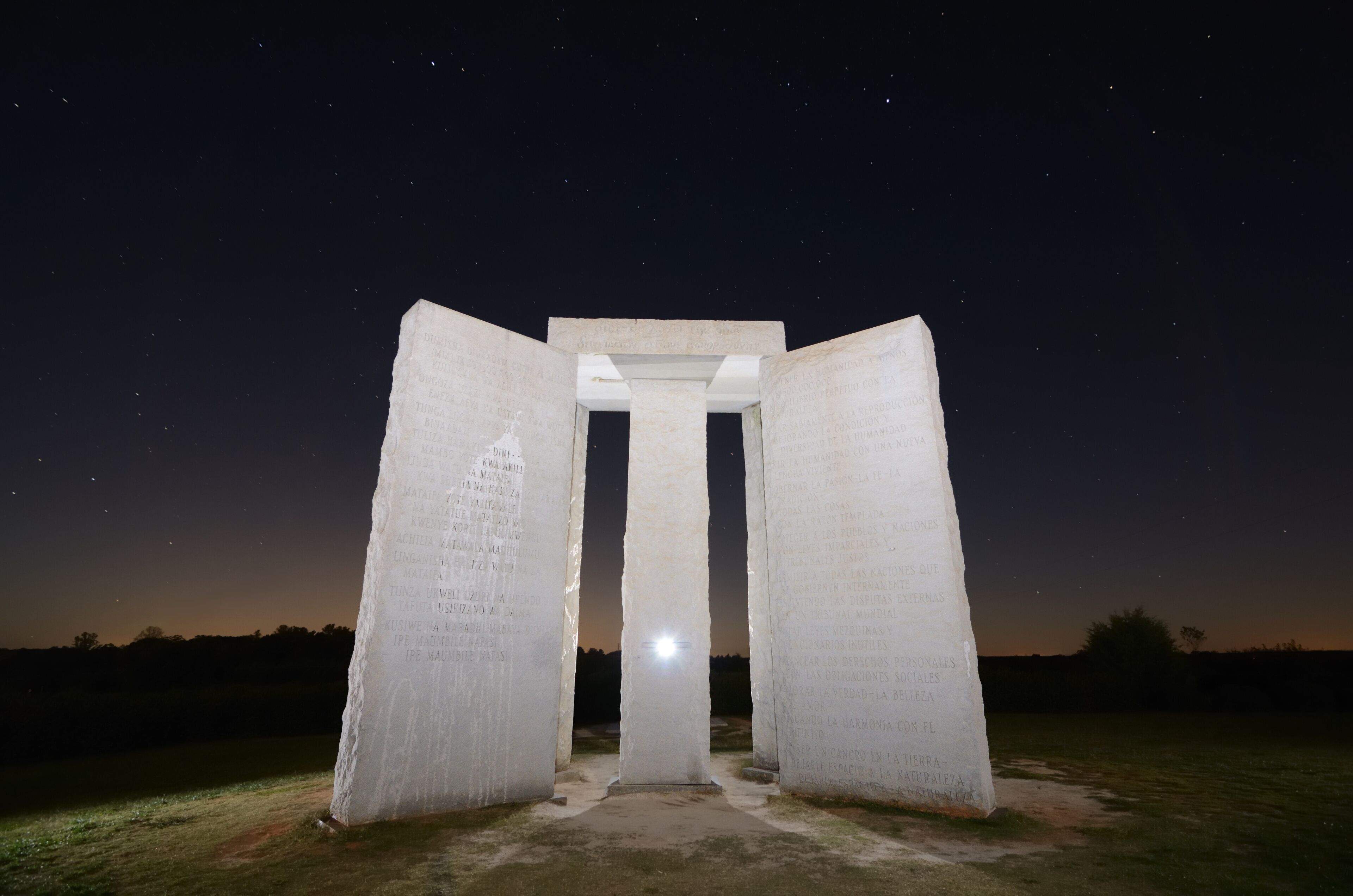 A large stone monument with inscriptions, set against a night sky with stars.