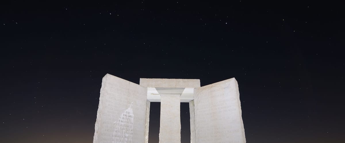 A large stone monument with inscriptions, set against a night sky with stars.
