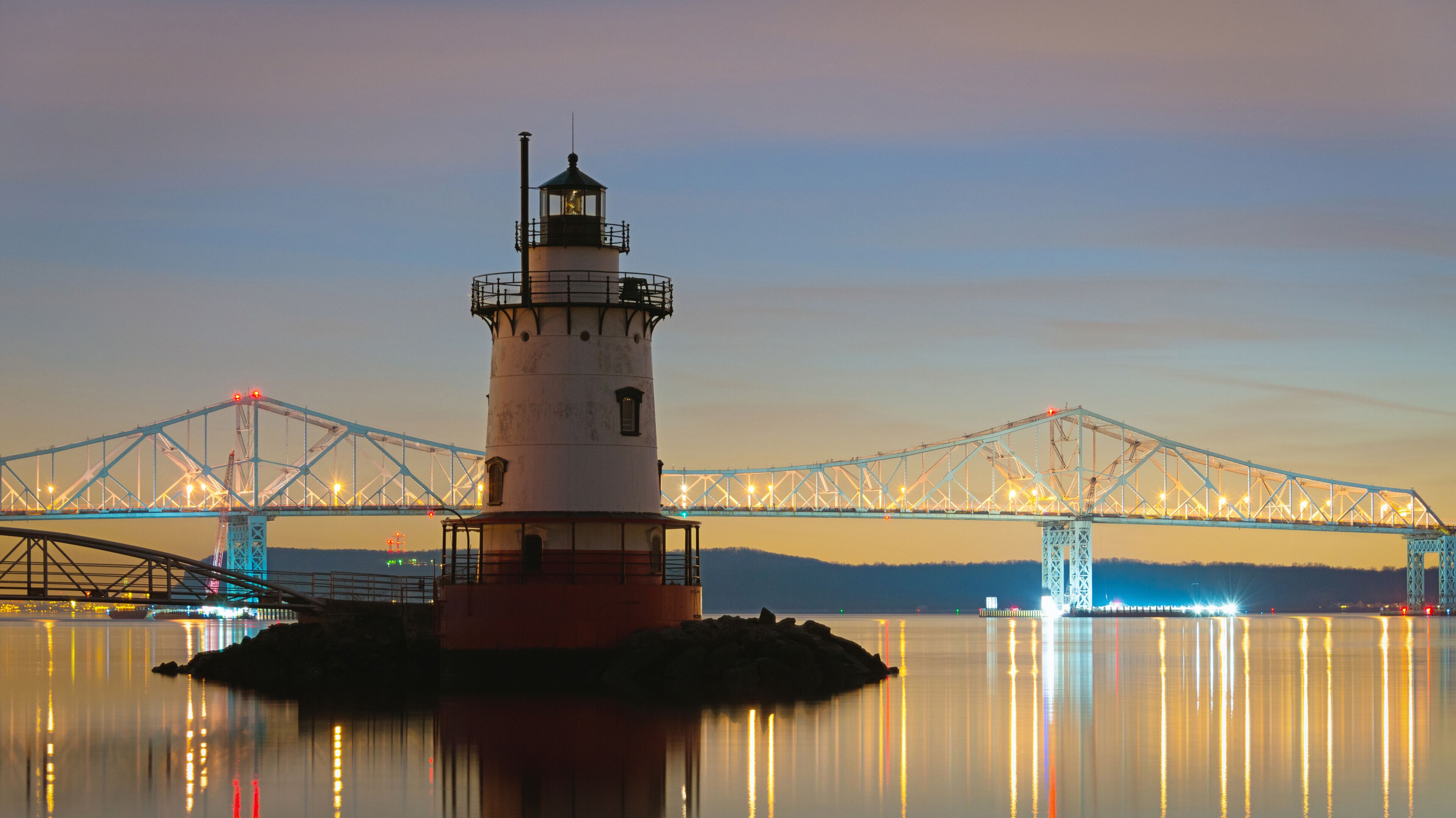 A lighthouse on a small island with a bridge in the background.