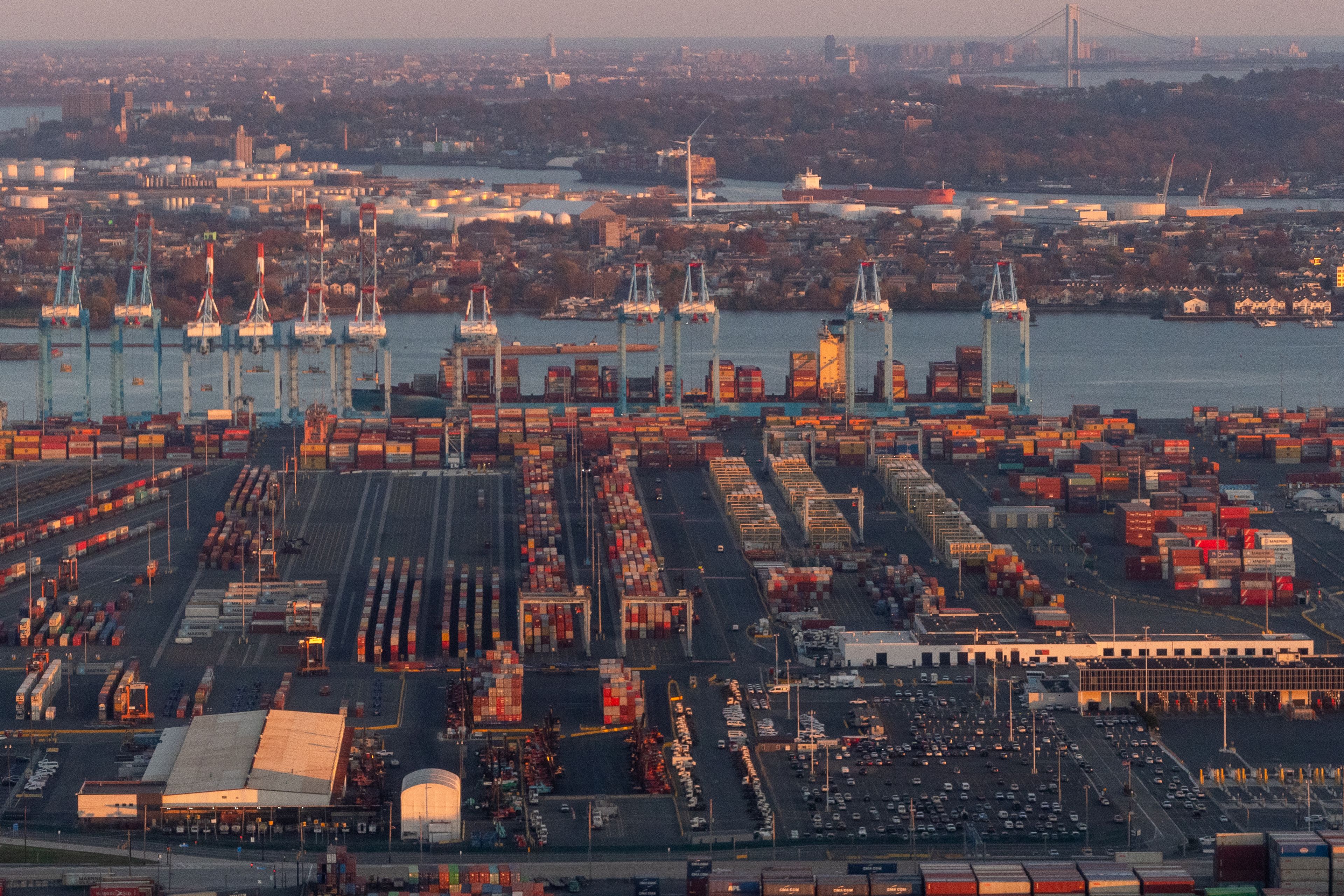 Port of Newark, Newark, New Jersey, USA - November 19, 2023 - Aerial view of Port Newark-Elizabeth Marine Terminal at dusk with shipping containers, gantry cranes and the Verrazano Narrows Bridge