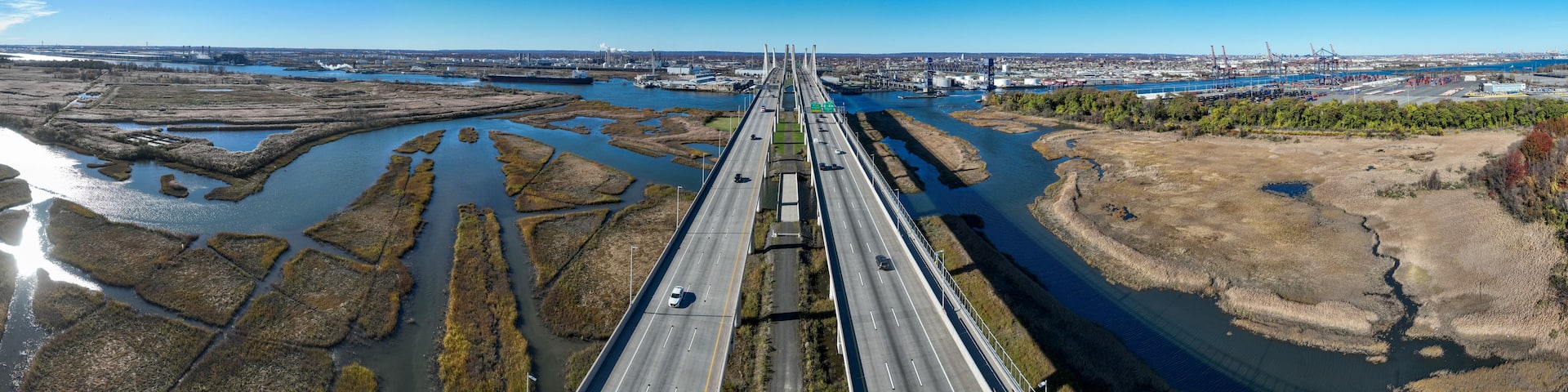 A bridge spanning a river with industrial facilities and a cityscape in the background.