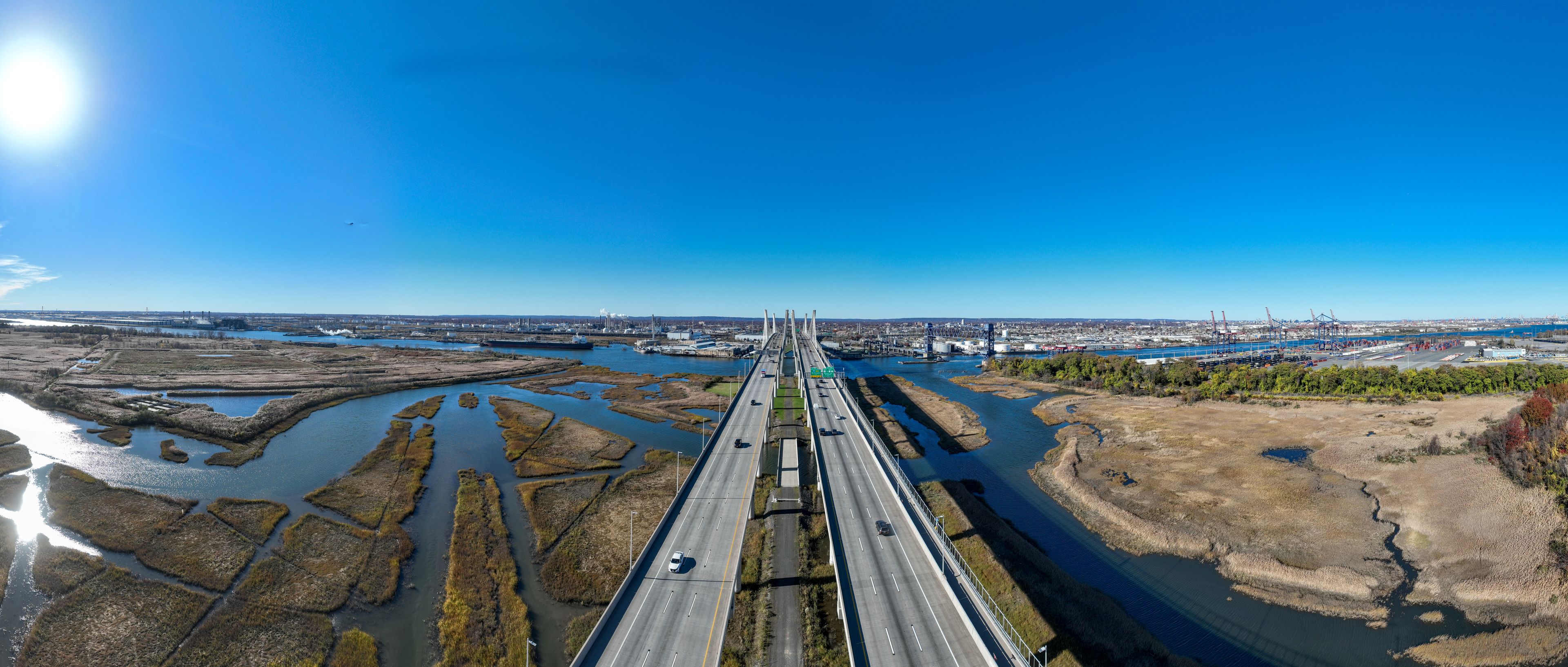 A bridge spanning a river with industrial facilities and a cityscape in the background.
