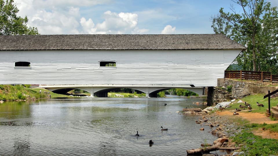 A covered bridge over a river with ducks swimming.
