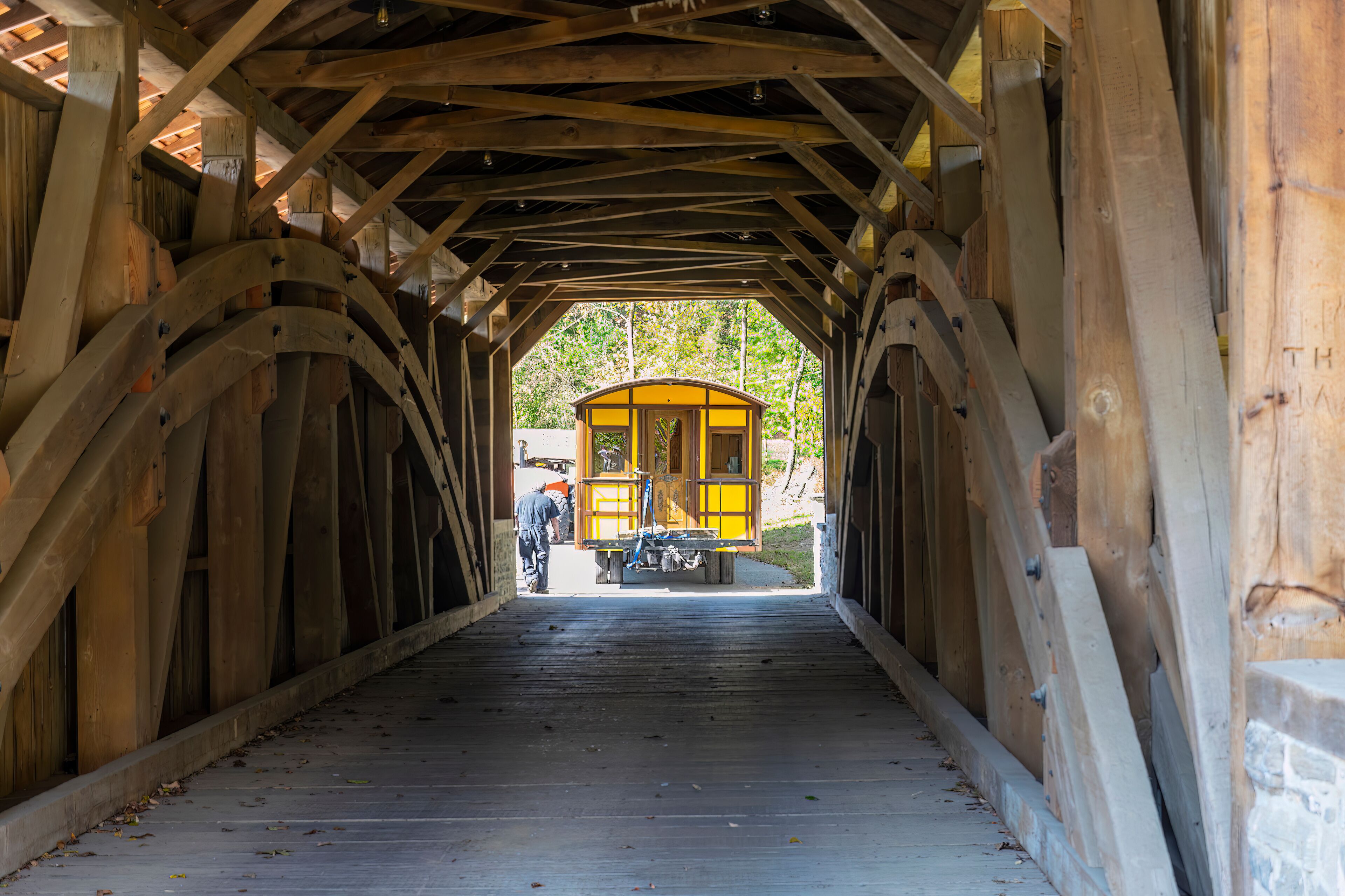 Installing a New Yellow Passenger Antique Coach Thru a Cover Bridge on to a Railroad Track on a Fall Day