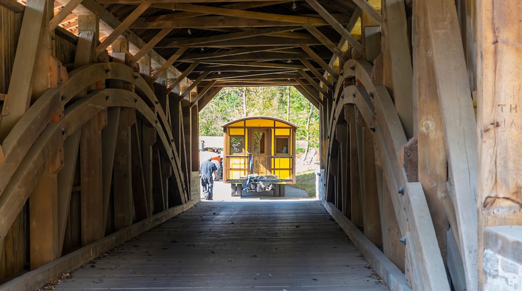 Installing a New Yellow Passenger Antique Coach Thru a Cover Bridge on to a Railroad Track on a Fall Day