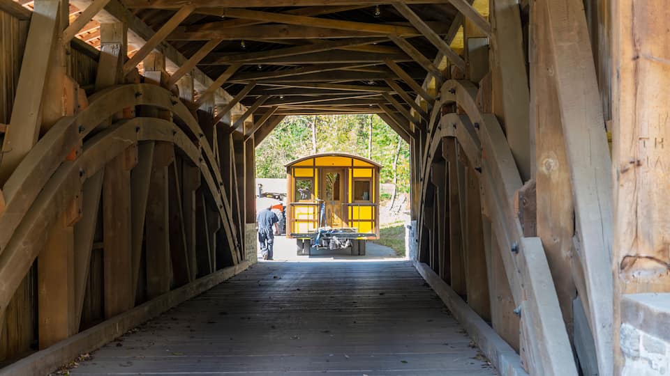 A wooden covered bridge with a yellow structure at the end.