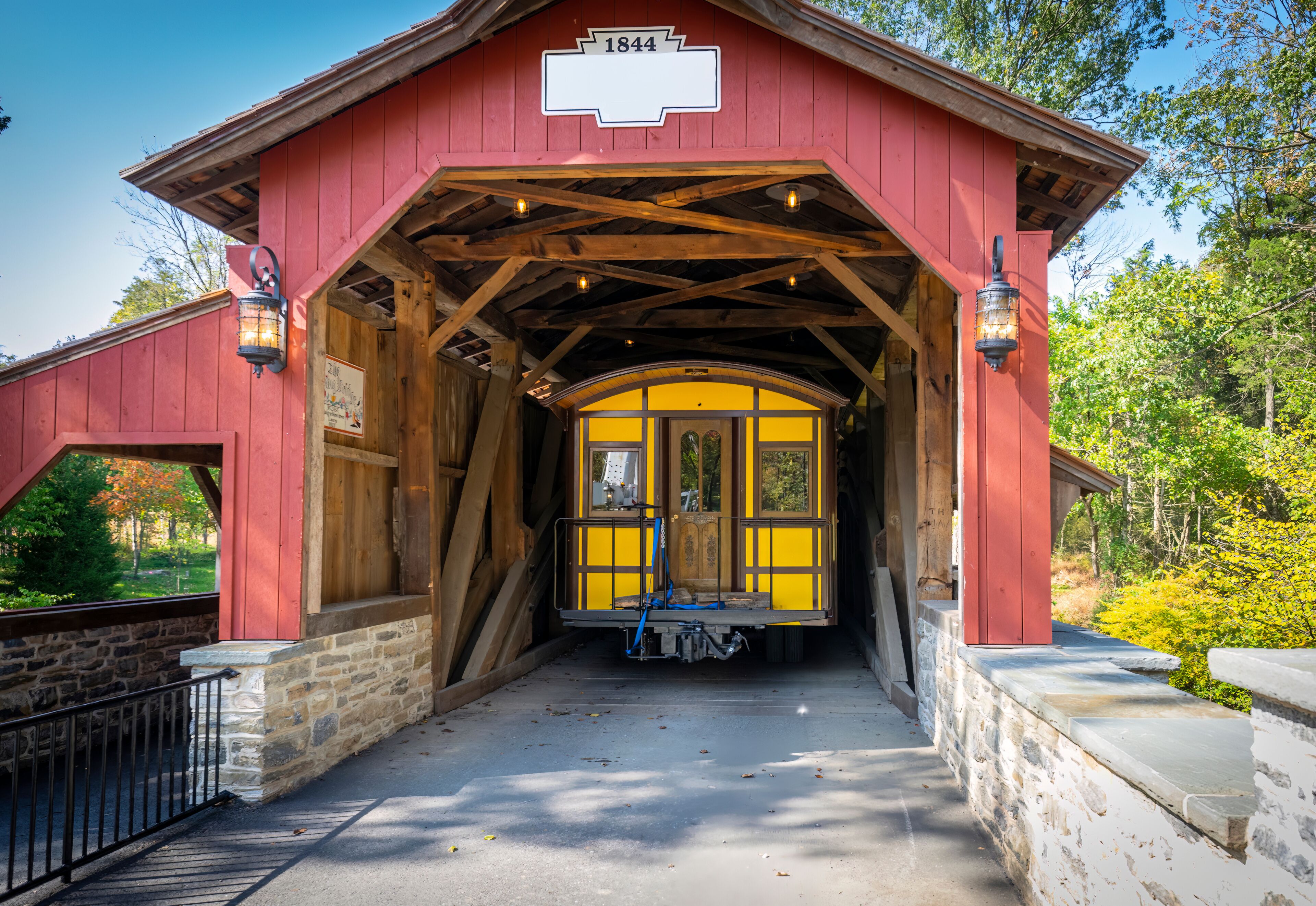 Installing a New Yellow Passenger Antique Coach Thru a Cover Bridge on to a Railroad Track on a Fall Day