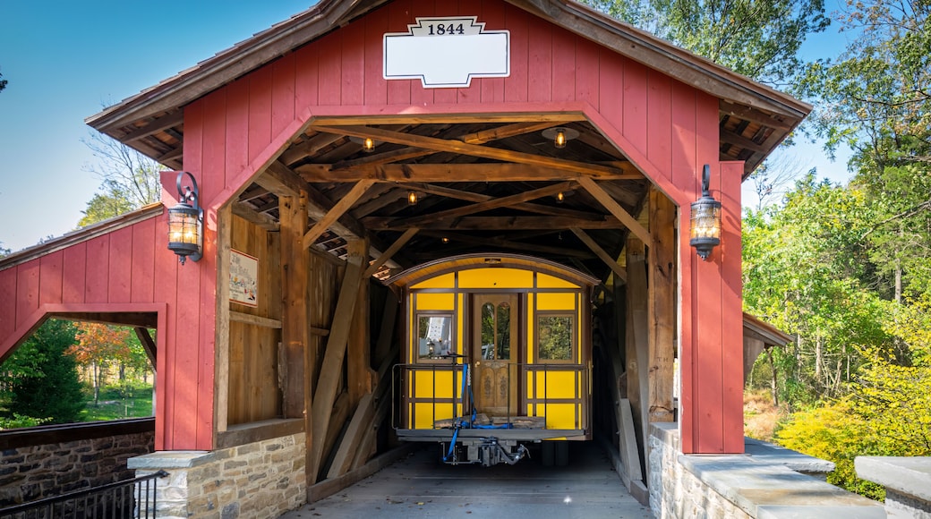 Installing a New Yellow Passenger Antique Coach Thru a Cover Bridge on to a Railroad Track on a Fall Day