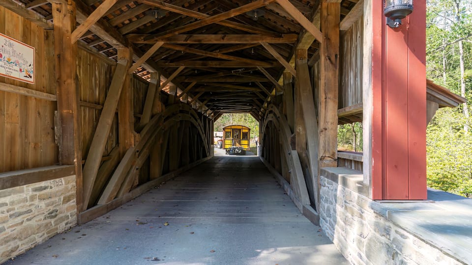 A covered wooden bridge with a yellow train in the distance.