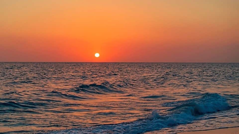 A sunset over a calm sea with waves gently lapping onto the shore.