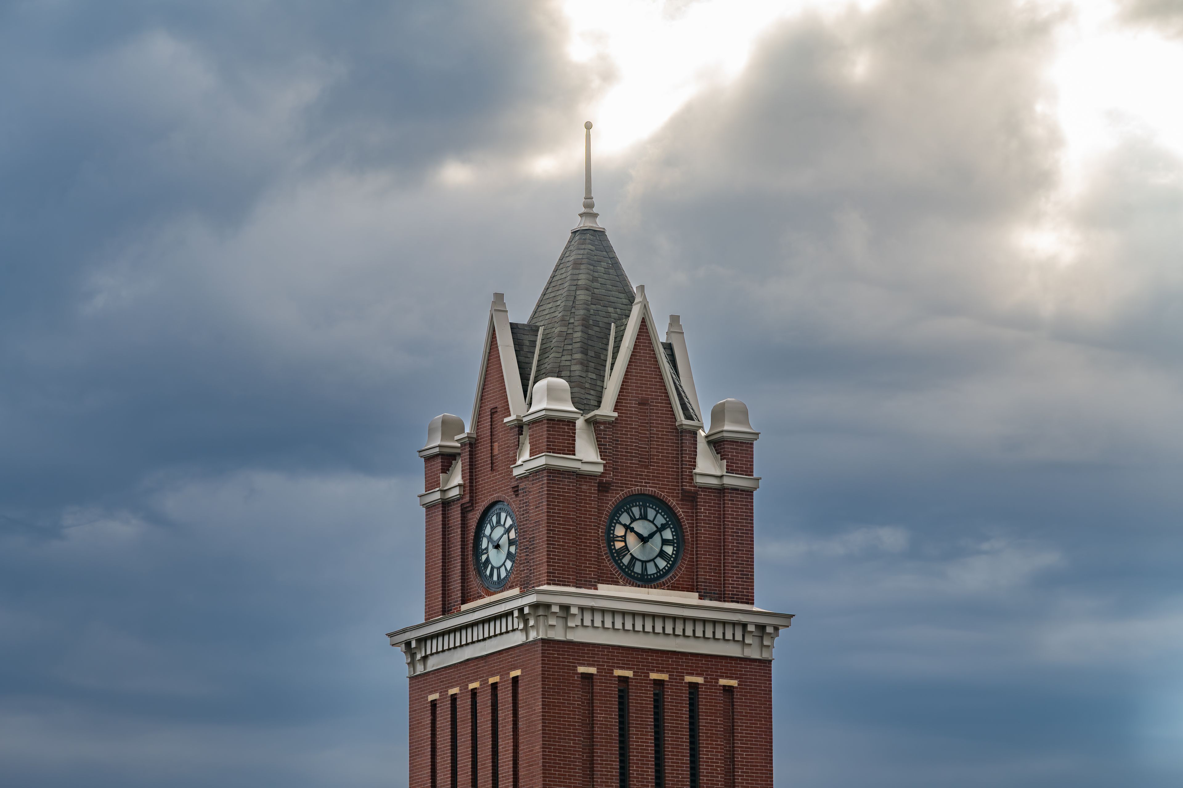 A clock tower with a pointed roof and two clocks on its side.