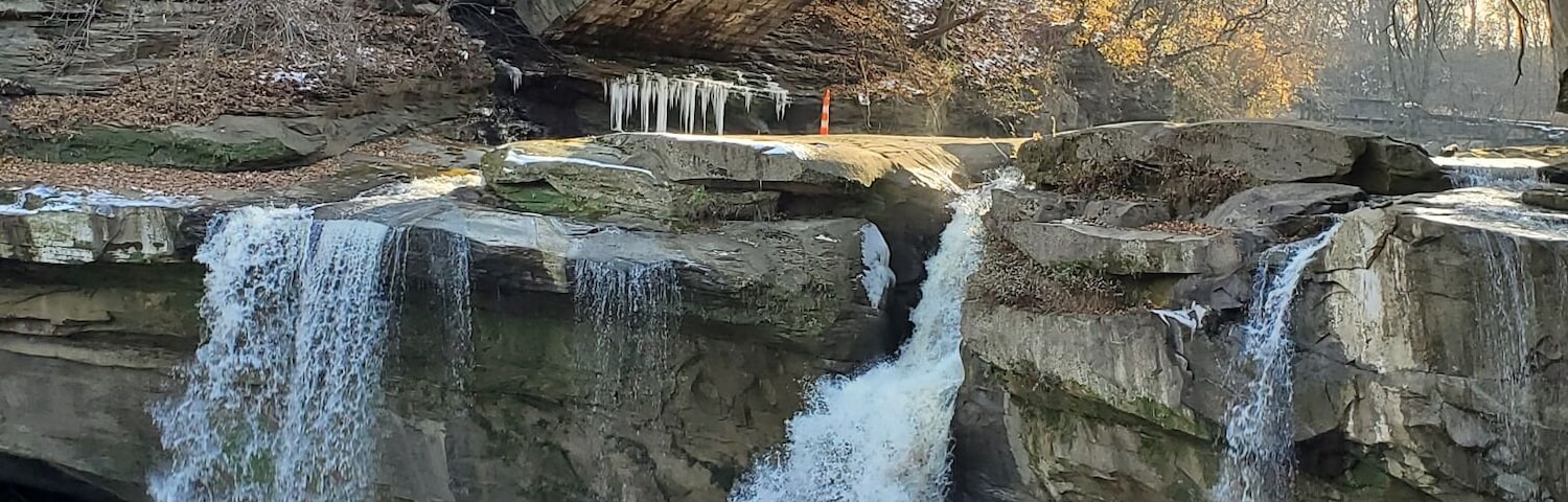 Una cascada se precipita sobre terreno rocoso, con un puente al fondo.