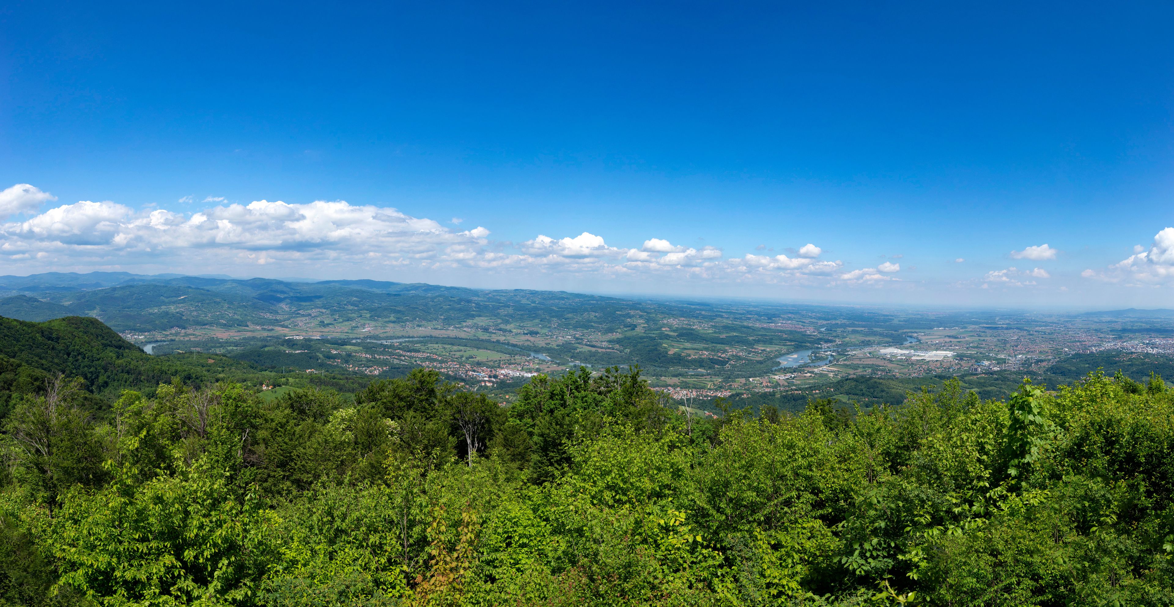 A panoramic view of a mountainous landscape with a river, dense forests, and a distant town.