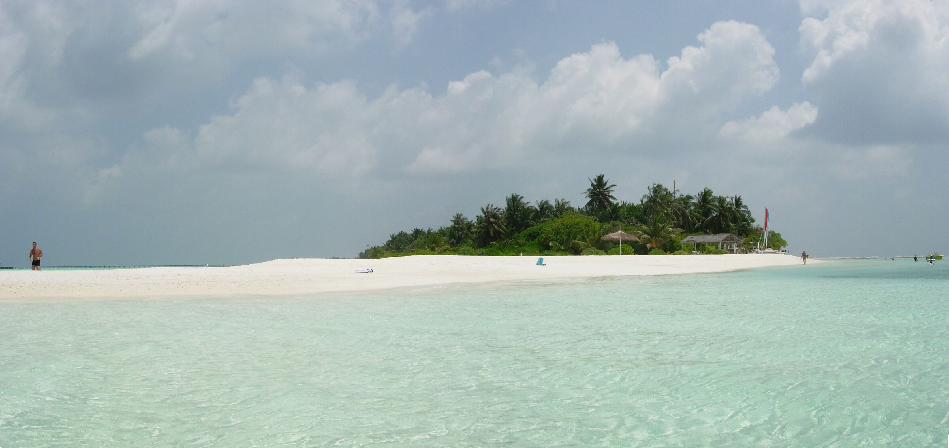 A beach with clear turquoise water, a white sandy shore, and a small island with palm trees and a hut.
