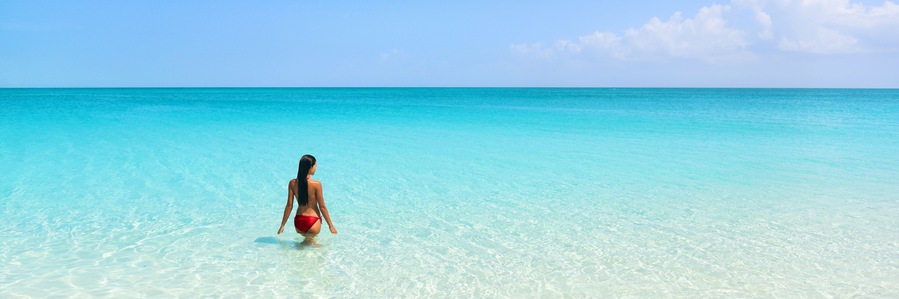 Beach luxury travel getaway resort vacation banner. Bikini woman relaxing enjoying tropical holidays swimming in turquoise ocean water in paradise destination.