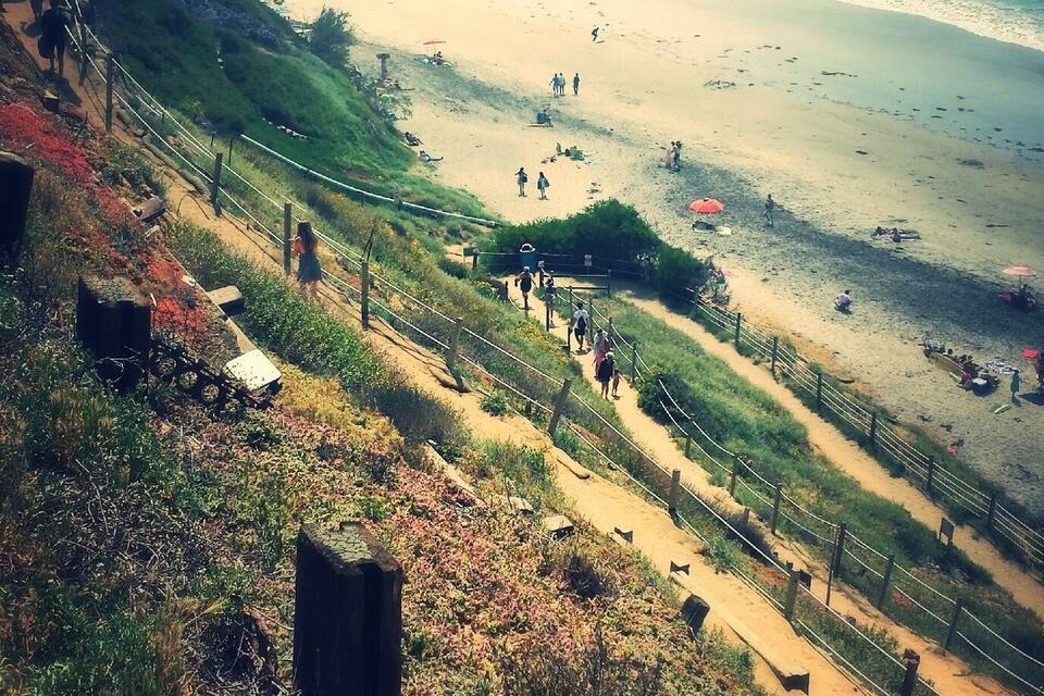 Paisatge costaner amb una platja sorrenca, un turó verd i una vista clara de l'oceà.
