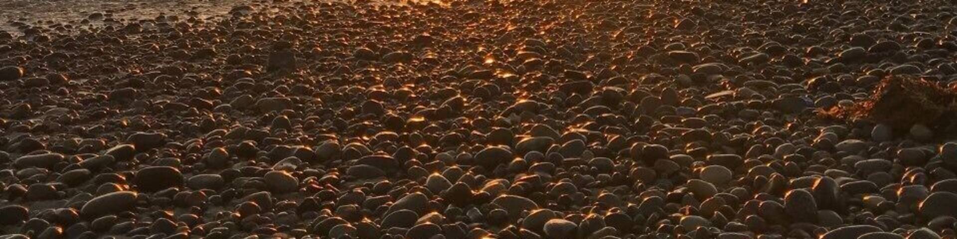 Atardecer sobre una playa de guijarros con el sol cerca del horizonte.