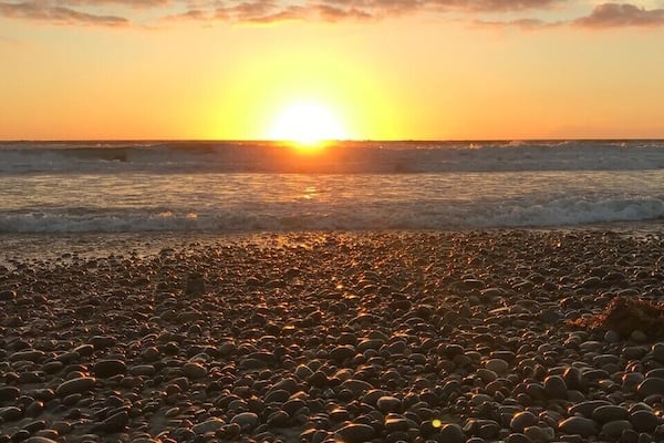 Um pôr do sol sobre uma praia de pedras, com o sol baixo no horizonte.