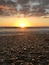 A sunset over a pebble beach with the sun low on the horizon.
