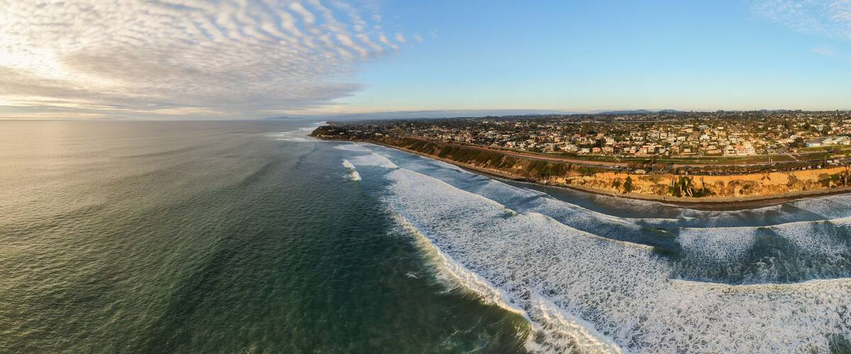 A coastal cityscape with a beach, ocean waves, and a clear sky.
