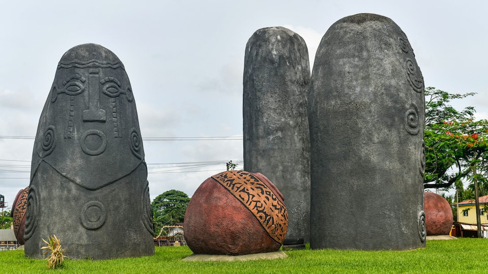 Three large stone sculptures with intricate carvings on a grassy field.