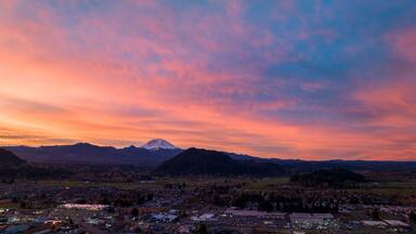 Aerial view of the town basking in the warm glow of the sunset, with Mount Rainier silhouetted against the vibrant sky, Enumclaw, Washington, United States.