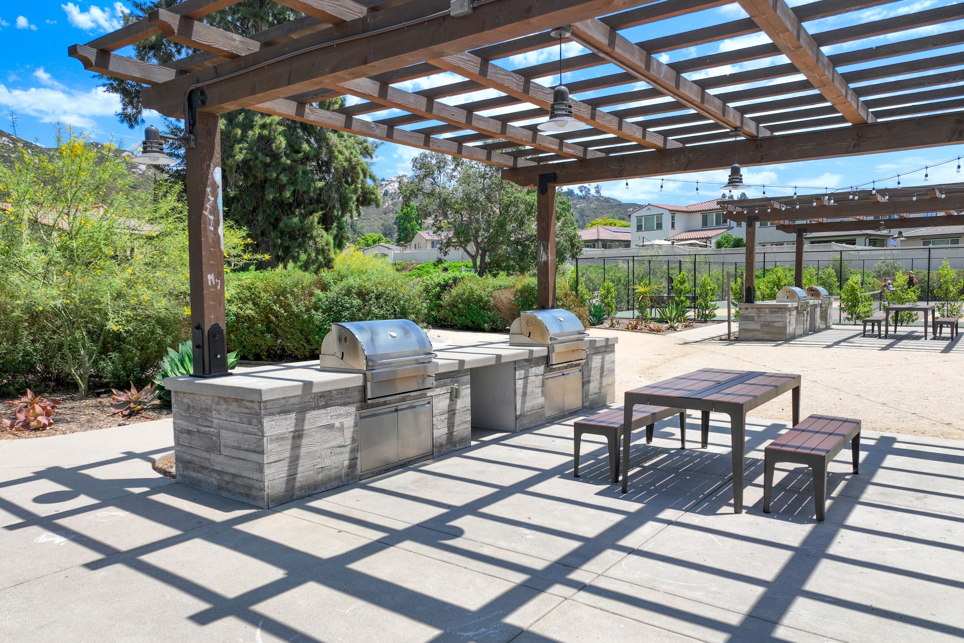 An outdoor patio with a pergola, stone barbecue station, and seating area.