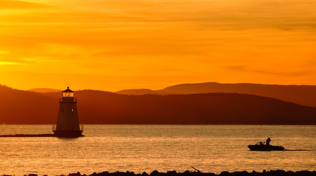 Golden sunset on Lake Champlain looking west towards the Adirondack Mountains of New York. Lighthouse and boat with fishermen in silhouette.