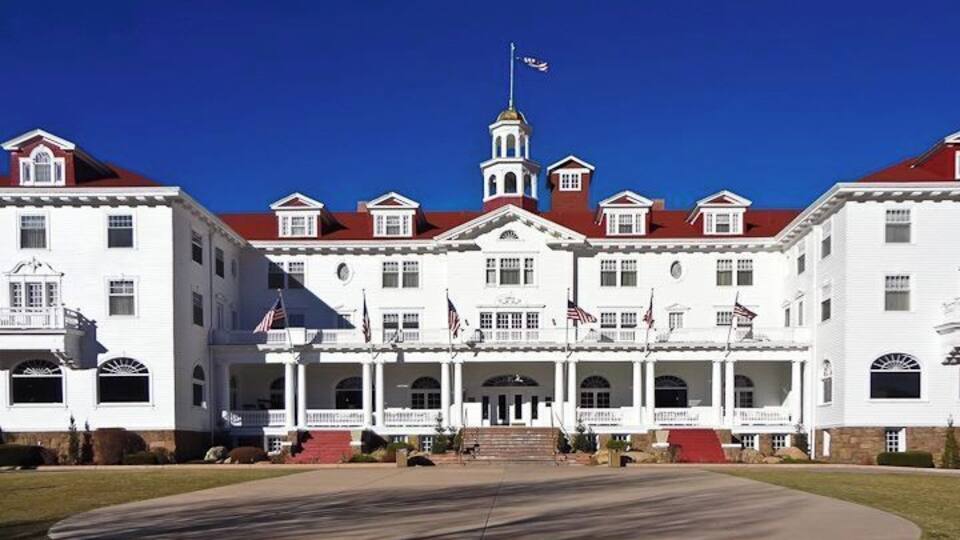 A large white building with a red roof, multiple flags, and a central tower.