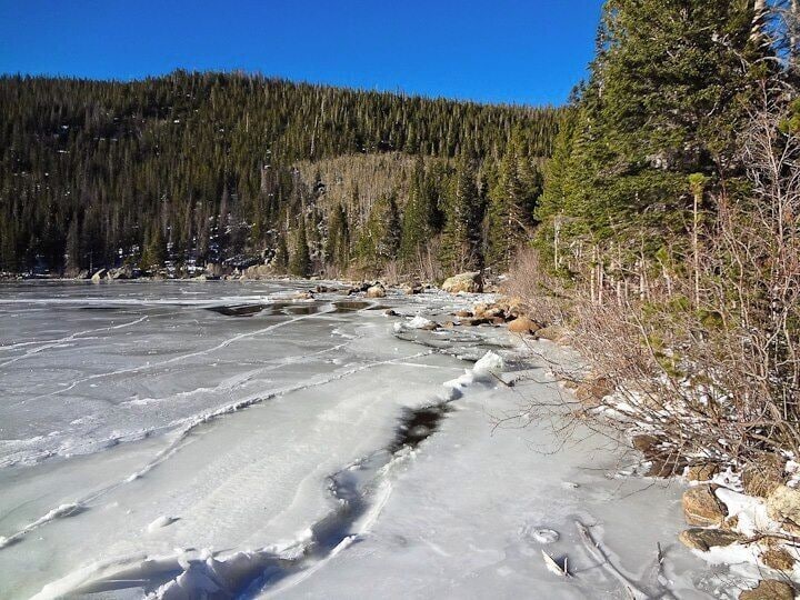 A frozen river with ice formations and a forested hillside in the background.