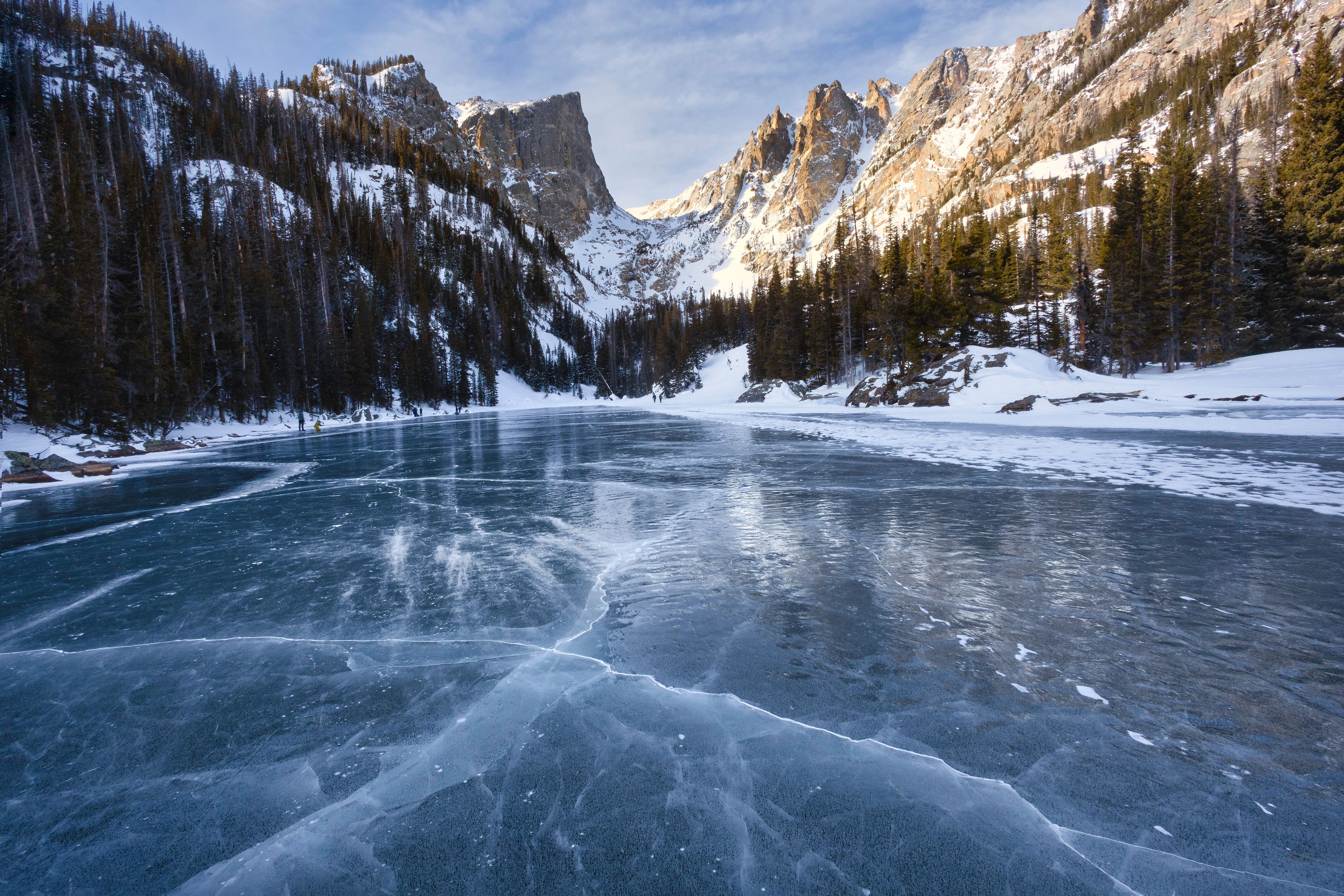 A frozen lake surrounded by snow-covered mountains and dense forests.