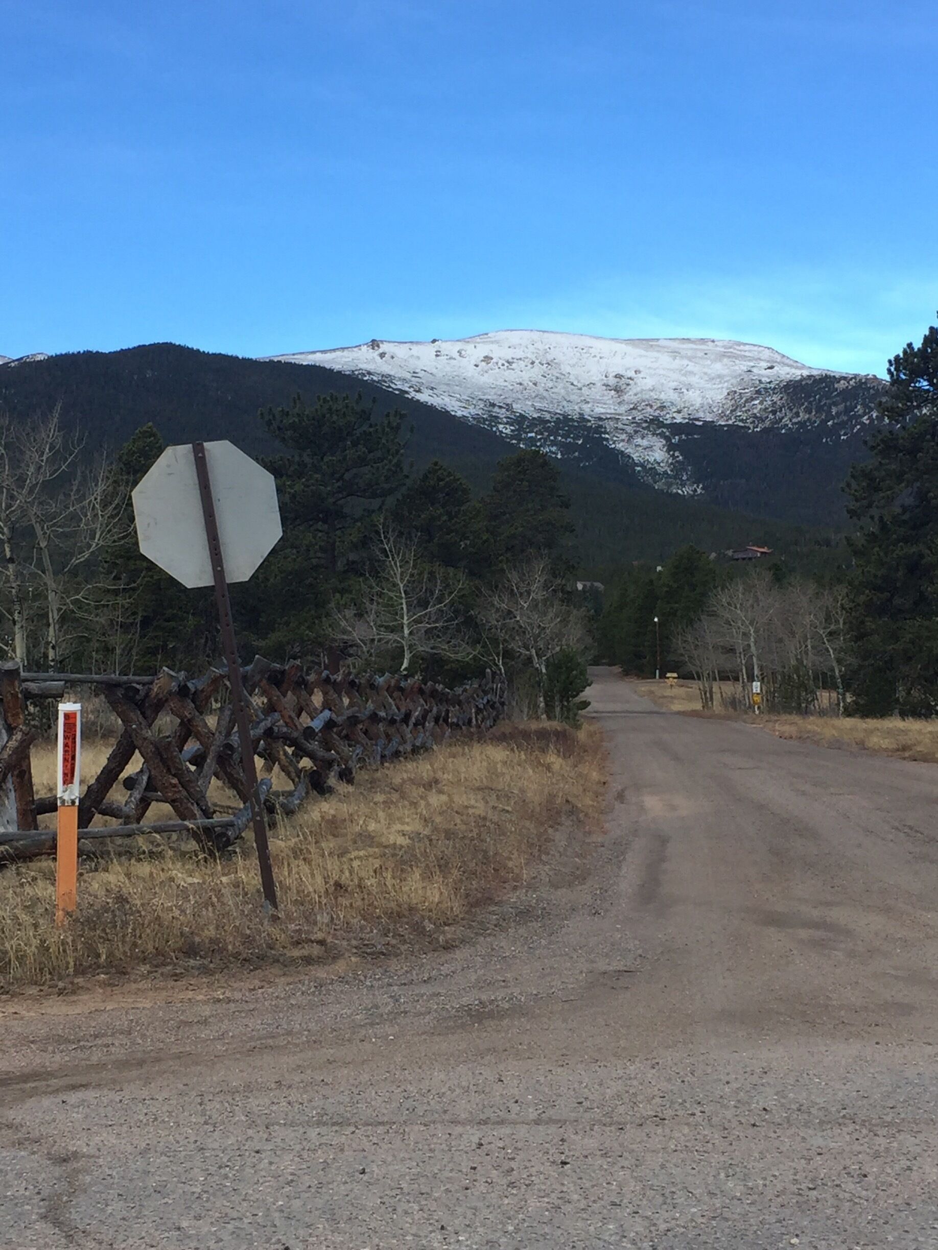 A road leading to a snow-capped mountain with a stop sign and a wooden fence on the left.