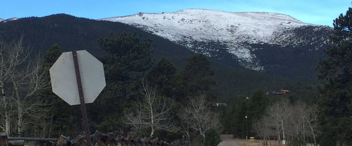 A road leading to a snow-capped mountain with a stop sign and a wooden fence on the left.