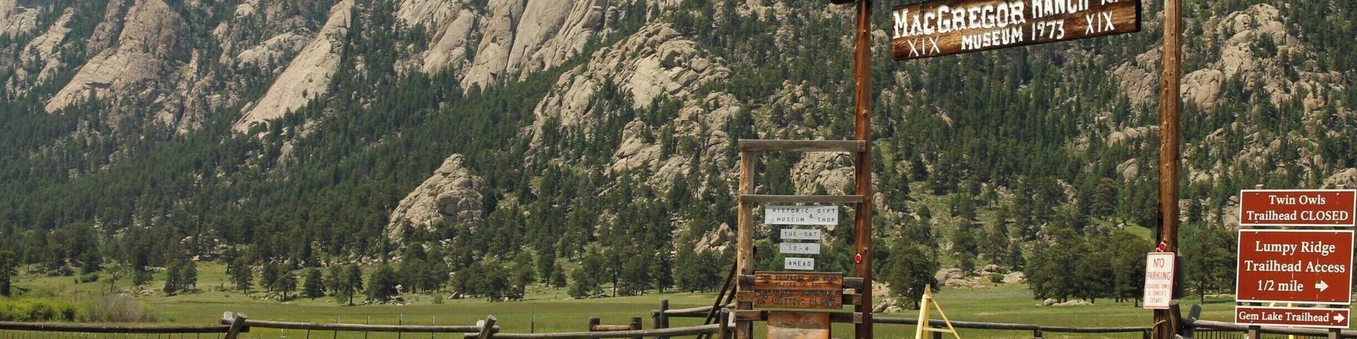 A signpost with 'MacGregor Ranch 1873' and 'Museum 1873' written on it, set against a mountainous backdrop.