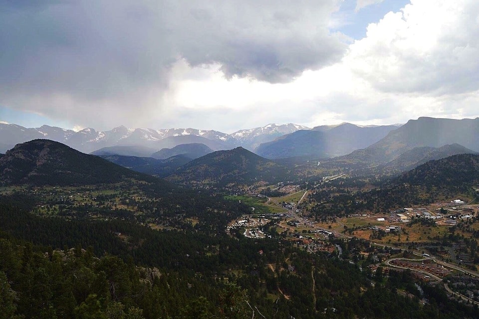 Paesaggio montuoso con un paese situato in una valle, circondato da fitte foreste e cime innevate all'orizzonte.